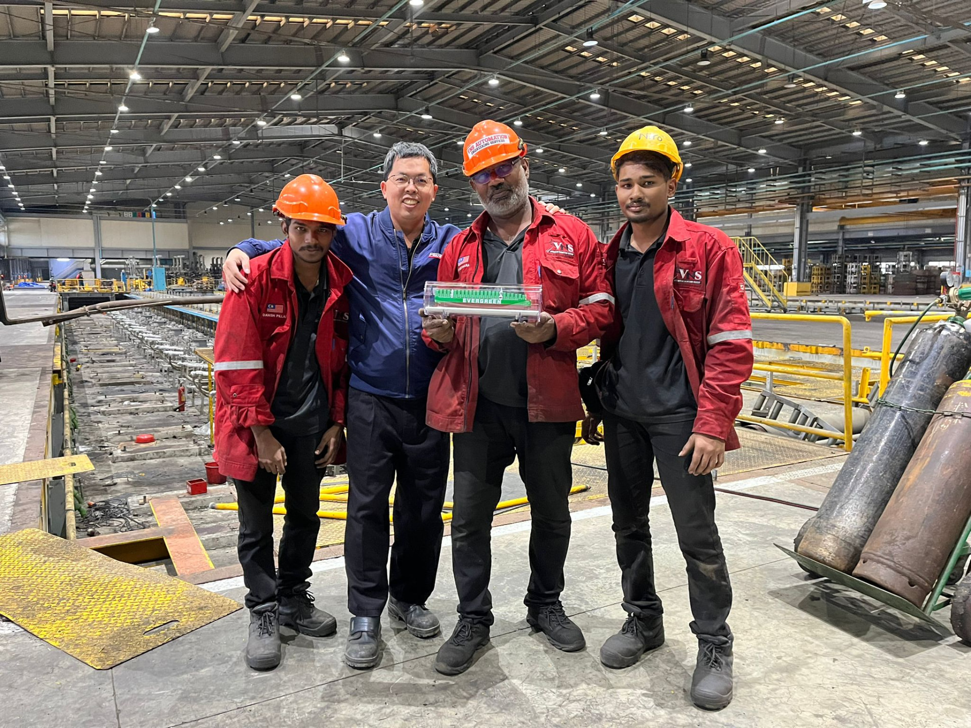 Four people wearing safety helmets and work clothing at an industrial facility